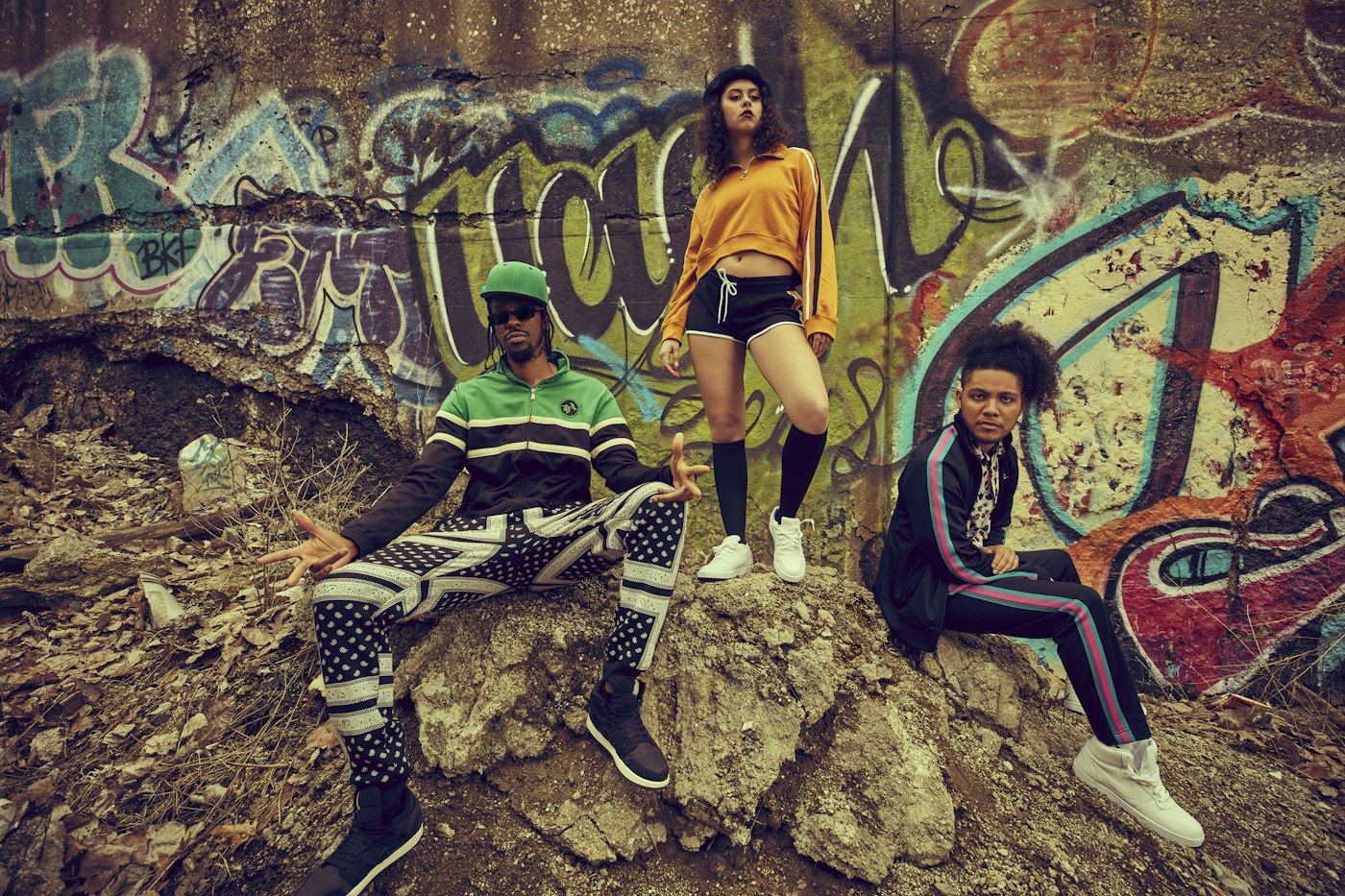 Three people in colour-blocked track jackets and retro streetwear against a graffiti wall